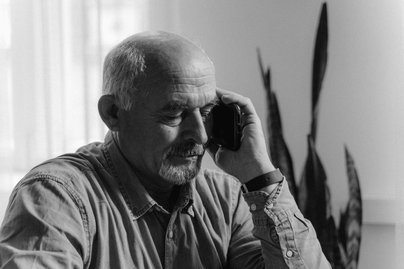 Homme âgé assis dans son salon, en conversation avec un proche, la main portée près de l'oreille